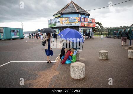 Urlauber trotzen den Elementen am Goodrington North Beach in Paignton, Devon, der von Gewitterschauern getroffen wurde und einige Touristen dazu zwingt, für Deckung zu laufen, Großbritannien. Stockfoto