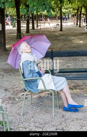 Dame, die unter einem lila Regenschirm auf einem Stuhl im Jardins du Luxembourg in Paris sitzt Stockfoto