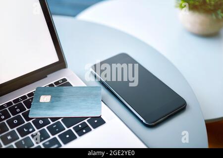 Laptop, elektronische Chipkarte und Smartphone auf blauem Rundtisch. Online-Zahlung oder Kundenidentifikation. Moderne Technologie, drahtlose Geräte und Transf Stockfoto