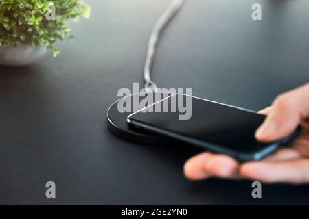 Mann, der das Smartphone im Büro auf ein drahtloses Induktionsladegerät legt. Grauer Tischhintergrund. Moderne Technik, drahtlose Geräte und Übertragung von energ Stockfoto