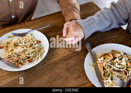 Nahaufnahme eines glücklichen, vielfältigen Paares im Wohnzimmer, das gemeinsam das Abendessen mit den Händen isst Stockfoto
