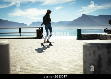 Gemischtes Rennen Frau Skateboarding an sonnigen Tag am Meer Stockfoto