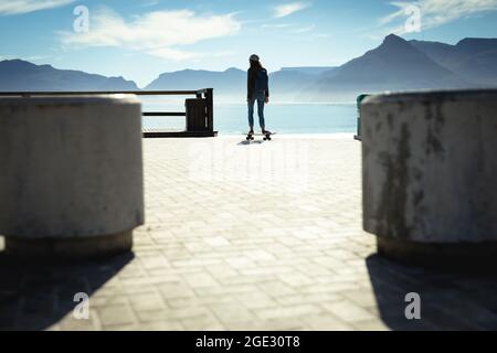 Gemischtes Rennen Frau Skateboarding an sonnigen Tag am Meer Stockfoto