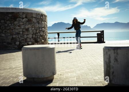 Gemischtes Rennen Frau Skateboarding an sonnigen Tag am Meer Stockfoto