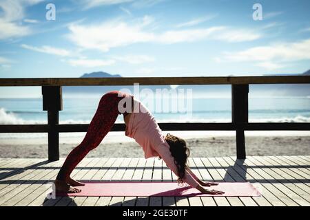 Frau mit gemischter Rasse, die an sonnigen Tagen am Meer Yoga praktiziert Stockfoto