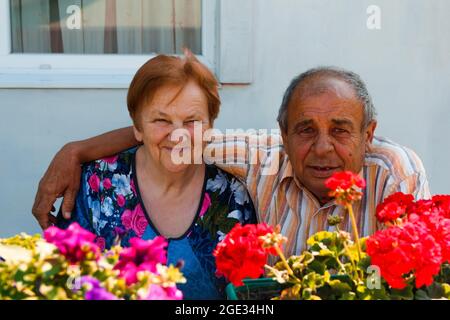 Ein älteres Paar, das sich am Sommertag umarmt. Fröhliche nette ältere Paar von Mann und Frau lächeln und posieren auf Blumen Garten Hintergrund. Liebe und Familie Stockfoto