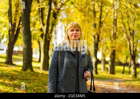 Unschärfe-Außenportrait der positiven selbstbewussten reifen Frau. Lächelnde weibliche Blondine. Elegante Frau mittleren Alters im Herbstpark. Nicht fokussiert. Stockfoto