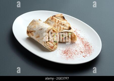 Shawarma- oder Pita-Rolle mit Fleisch und Gemüse auf weißem Teller auf grauem Hintergrund Stockfoto