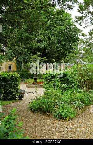 Englischer Country Garden in den Cotswolds im Sommer mit kleinem Wasser mit Springbrunnen und Schubkarre Stockfoto