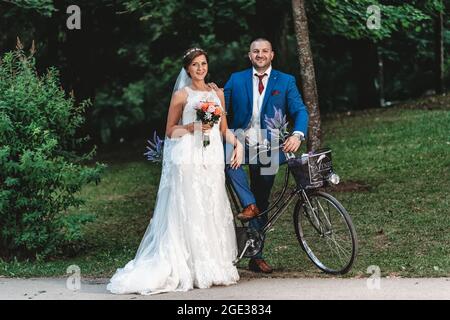 Schöne Braut im eleganten weißen Brautkleid mit langem Schleier und Bräutigam in blauem Anzug Stockfoto