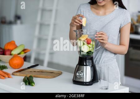 Teilansicht einer lächelnden Frau, die mit Zucchini in Scheiben Apfel in den elektrischen Mixer gegeben hat Stockfoto