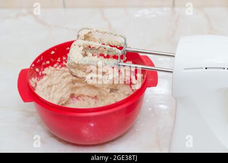 Elektrischer Quirl auf einer roten Schüssel mit Teig Stockfoto