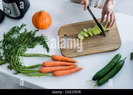 Teilansicht einer Frau, die Zucchini auf einem Schneidebrett in der Nähe von frischem Gemüse in der Küche schneidet Stockfoto