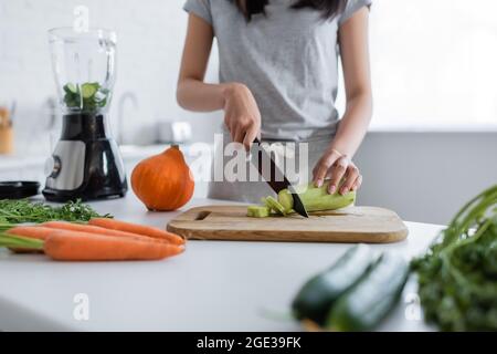 Beschnittene Ansicht einer Frau, die frische Zucchini in der Nähe von elektrischem Shaker und Gemüse schneidet Stockfoto