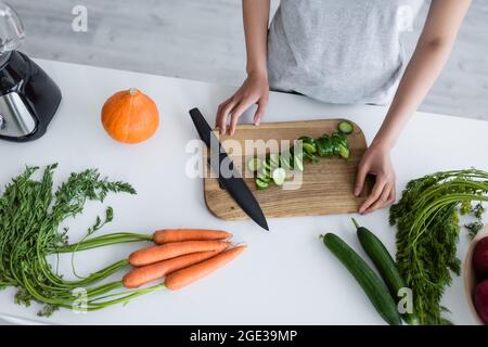 Teilansicht einer Frau in der Nähe des Schneidebretts mit in Scheiben geschnittenen Gurken, Karotten und Kürbis auf dem Tisch Stockfoto