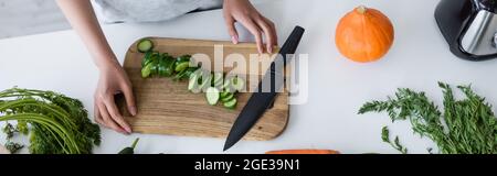 Teilansicht einer Frau in der Nähe von geschnittenen Gurken auf hackenden Wildschweinen und reifem Kürbis auf dem Tisch, Banner Stockfoto