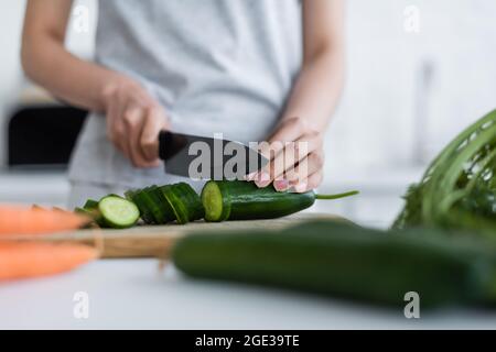 Teilansicht einer Frau, die frische Gurken auf unscharfem Vordergrund schneidet Stockfoto