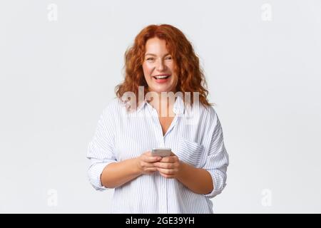 Porträt der Mutter, mittleren Alters Rotschopf Frau schreiben Nachricht, SMS mit Smartphone. Frau schaute auf die Kamera, hielt Handy und lächelte glücklich Stockfoto