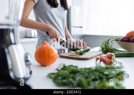 Teilansicht einer Frau, die in der Nähe von Kürbis Gurken schneidet, und Karotten auf verschwommenem Vordergrund Stockfoto