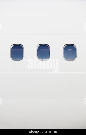 Drei Fenster auf dem Rumpf eines weißen Flugzeugs. Vertikales Bild der Ebene mit Kopierbereich. Stockfoto