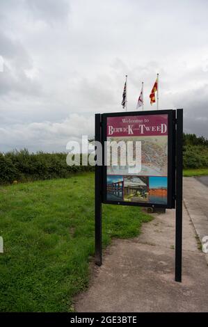 Berwick upon Tweed-Schild an der englischen Grenze zu Schottland. Flaggen im Hintergrund, Gras und Pfad unten und zur Seite des Schildes. Keine Personen. Stockfoto