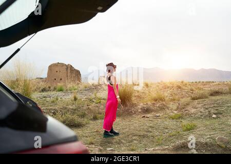 Junge asiatische Frau Autoreisende in roten Kleid genießen die Morgensonne auf der Straße Stockfoto