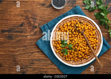 Gebratene Kichererbsen mit Kurkuma in Keramikplatte auf einem alten Holztisch Hintergrund. Geröstete, würzige Kichererbsen oder indische Chana oder chole, beliebter Snack reci Stockfoto