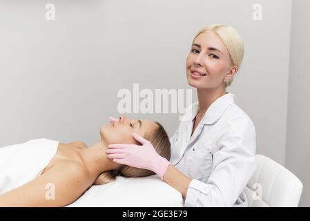 Kosmetikerin in Gummihandschuhen gibt dem Kunden eine Anti-Aging-Massage in einem Schönheitssalon, mit Blick auf die Kamera. Stockfoto