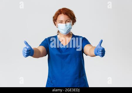 Medizinisches Personal, covid-19 Pandemie, Coronavirus Konzept. Glücklich lächelnde Ärztin, Krankenschwester mittleren Alters in medizinischer Maske und Handschuhe zeigen Daumen-up Stockfoto