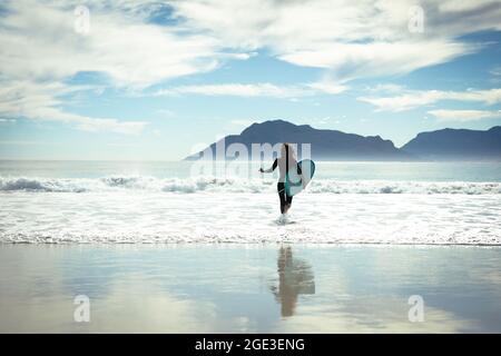 Frau mit gemischtem Rennen, die an einem sonnigen Tag Surfbrett im Meer hält Stockfoto