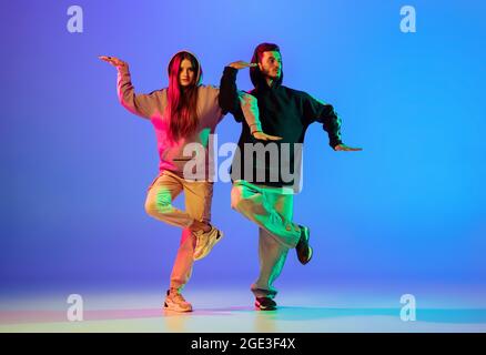 Zwei junge Menschen, Mann und Frau, tanzen brakedance, Hip-Hop auf blauem Hintergrund in Neonlicht. Stockfoto