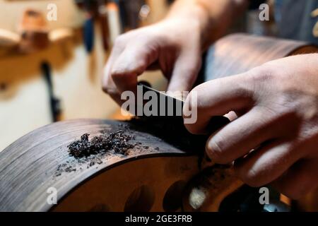 Unbekannter Geigenbauer, der in seiner Werkstatt eine Gitarre schleift und Werkzeuge verwendet. Stockfoto