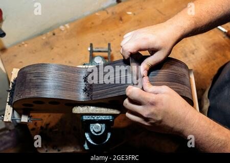 Unbekannter Geigenbauer, der in seiner Werkstatt eine Gitarre schleift und Werkzeuge verwendet. Stockfoto