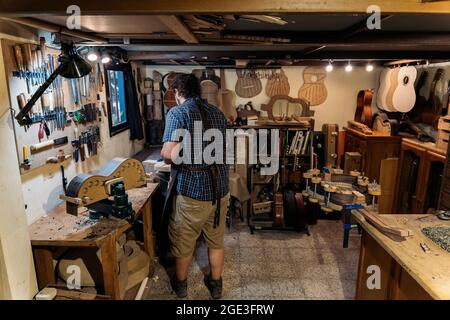 Unbekannter Geigenbauer, der eine Schürze trägt und eine Gitarre macht und in seiner Werkstatt arbeitet. Stockfoto