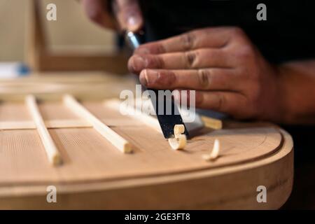 Unanerkannter Handwerker, der eine Gitarre kreiert und Werkzeuge in einer traditionellen Werkstatt verwendet. Stockfoto