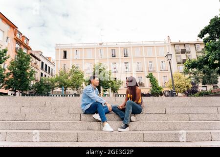Multikulturelle junge Freunde, die auf der Straße sitzen und sich unterhalten und angusten. Stockfoto