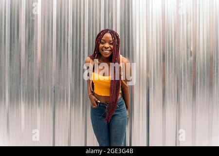 Schöne junge afrikanische Frau mit Zöpfen, die im Freien auf die Kamera schauen und lächeln. Stockfoto