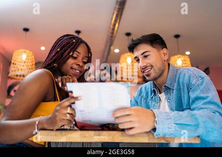 Multikulturelle Freunde sitzen in einem Restaurant und lesen gemeinsam das Menü. Stockfoto