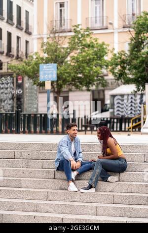 Multikulturelle junge Freunde, die auf der Straße sitzen und sich unterhalten und angusten. Stockfoto