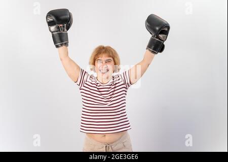 Eine ältere Frau mit Handschuhen hebt ihre Hände auf einen weißen Hintergrund. Sieg in einem Duell Stockfoto