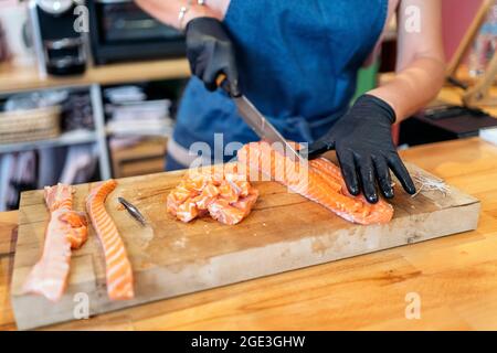 Nicht anerkannter Restaurantmitarbeiter trägt Latexhandschuhe und schneidet Lachs mit einem Messer. Stockfoto