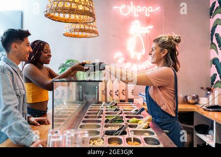 afroamerikanische Frau und ihre Freundin kaufen in einem coolen Restaurant eine Poke-Schale. Stockfoto
