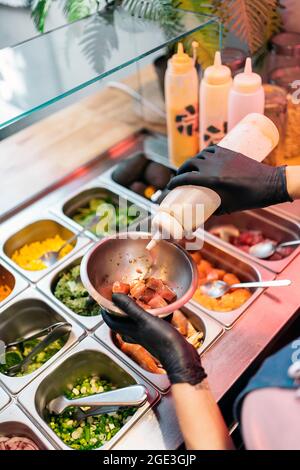 Nicht anerkannter Restaurantmitarbeiter in Schutzhandschuhen, der spezielle Sauce in eine Poke-Schüssel gegeben hat. Stockfoto
