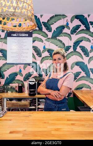 Blonde Frau mit Schürze lächelnd und Blick auf die Kamera während der Arbeit in einem Restaurant. Stockfoto