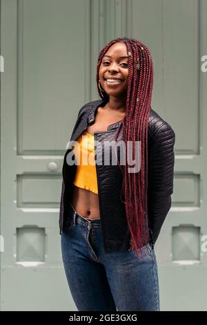 Schöne junge afrikanische Frau mit Zöpfen, die im Freien auf die Kamera schauen und lächeln. Stockfoto