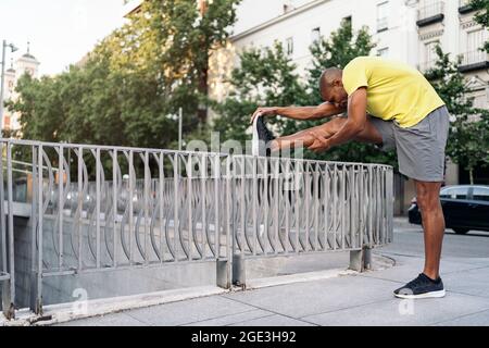Afroamerikanischer Mann, der sein rechtes Bein über das Geländer in der Stadt streckt, Stockfoto