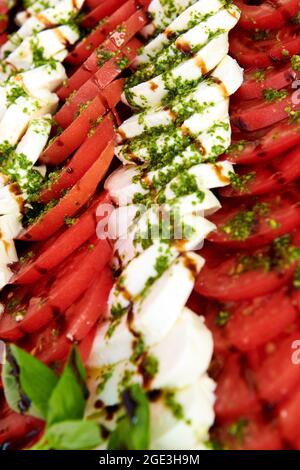 Caprese Salat Hintergrund. Viele Tomaten und Mozzarella-Käse in Scheiben geschnitten, mit Pesto-Sauce überzogen. Gesundes Lifestyle-Konzept Foto. Wunderschönes Catering Stockfoto