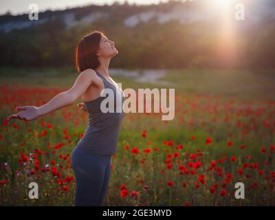 Junge schöne Frau mit erhobenen Armen im Frühjahr Mohnfeld. Sanfte Farben. Nachdenkliche, entspannte Atmosphäre. Stockfoto