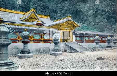 Alte japanische, handkolorierte Postkarte eines unbekannten japanischen Schreines, mit Haupteingangstor und dekorativer Wand und steinernen Laternen draußen. Ca. 1910. Stockfoto