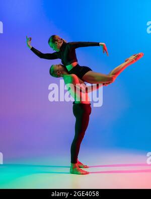 Stilvolles, sportliches kaukasisches Paar, männliche und weibliche Tänzerin, die zeitgenössischen Tanz auf farbenprächtigem blaurosa Hintergrund in Neonlicht tanzt. Stockfoto